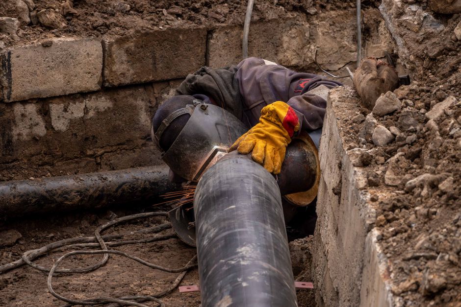 Close-up of a worker inspecting a drain pipe with tools in a garden setting near Crowborough